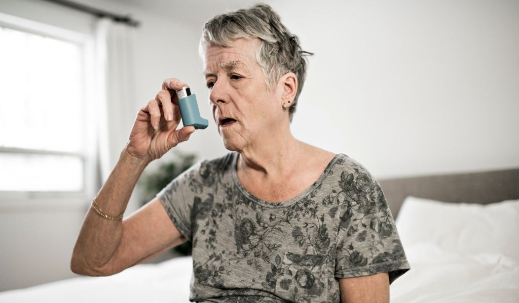 Elderly woman struggling to breathe properly whilst taking her asthma inhaler