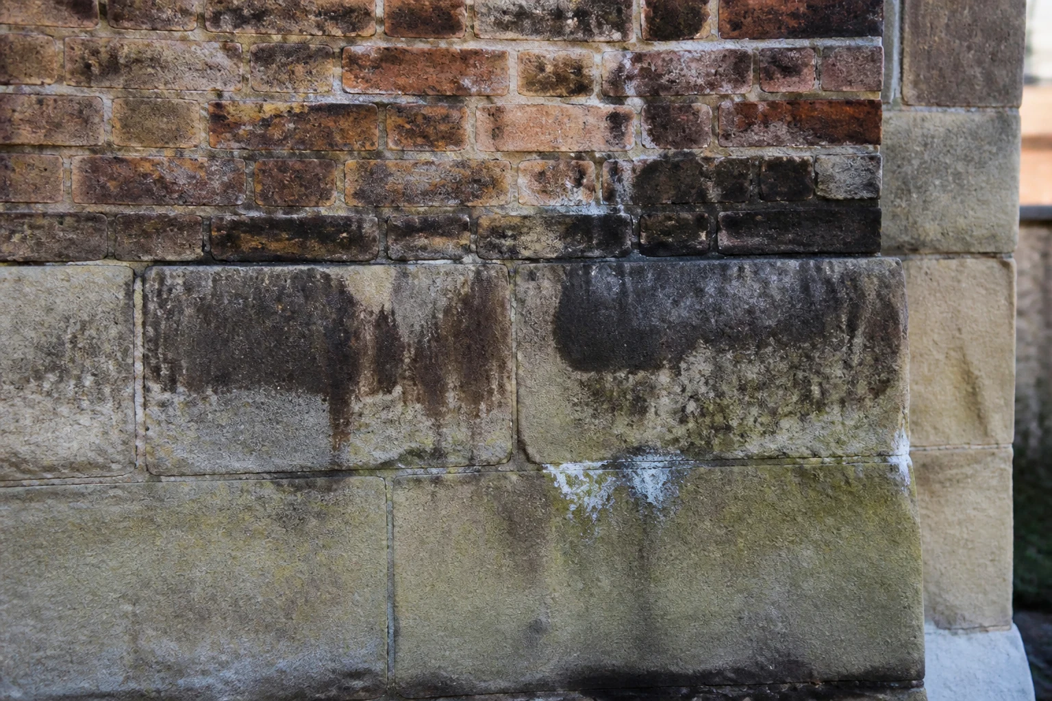 Weathered masonry wall with dark staining and mineral marks